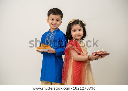 Siblings in ethnic wear smiling looking at the camera holding diya and ladoos Royalty-Free Stock Photo #1821278936