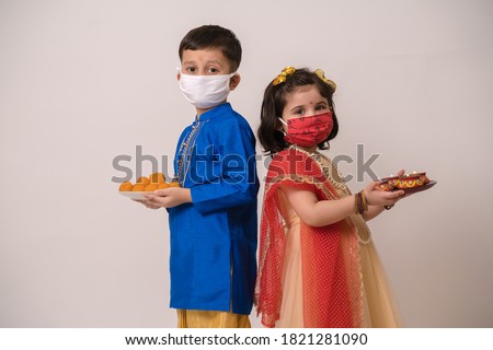 Siblings in ethnic wear, wearing mask celeberating festival holding diya and ladoos Royalty-Free Stock Photo #1821281090
