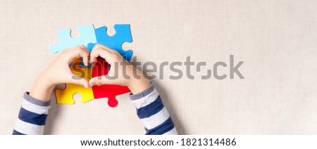 Beautiful banner - World autism awareness day, understanding  love concept, adorable hands of little child making heart shape over symbol colored puzzle. Autistic spectrum disorder, ASD, April 2.