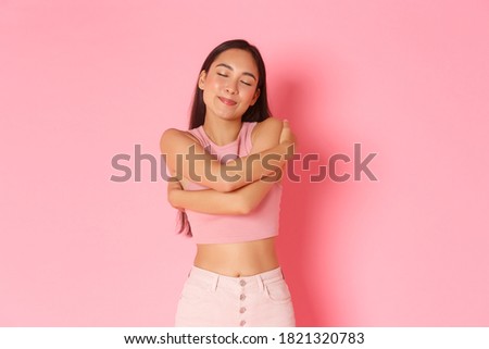 Lifestyle, beauty and women concept. Portrait of carefree, romantic asian girl smiling while daydreaming, close eyes and remember moment, hugging herself, standing over pink background Royalty-Free Stock Photo #1821320783