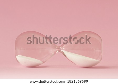 Hourglass lying on pink background - Concept of time and woman Royalty-Free Stock Photo #1821369599