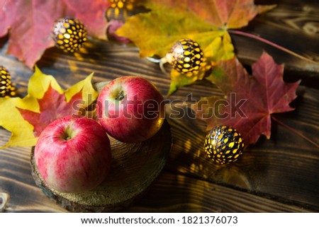 Pink ripe apples on a wooden table with fallen yellow and red maple leaves. Lights of garlands, warm and cozy autumn atmosphere, thanksgiving, harvest festival. Copy space