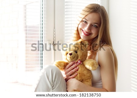 Smiling girl with a teddy bear at the window