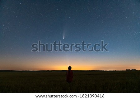 Silhouette of a man standing at night in a field outside the city. Starry night sky with comet Neowise C/2020 F3