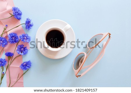 Top view of coffee cup, blue wild flowers, pink sunglasses and pink silk ribbon on a pastel blue background. Summer flatlay. Lifestyle, mock-up.