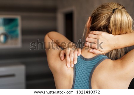 Sports injury concept. Athletic woman feeling pain in her neck against blurred background. Pain after home workout Royalty-Free Stock Photo #1821410372