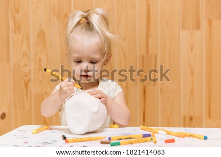 Little girl paints a piggy bank with markers