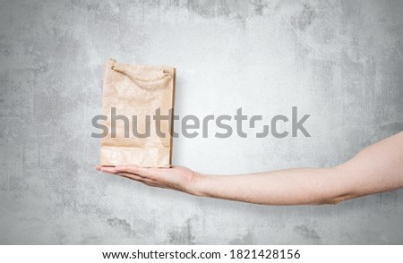Paper bag in hand on a stone background. Concept of using ecological items. The man holds a brown bag with a gift, purchases in his hand. Giving gifts.