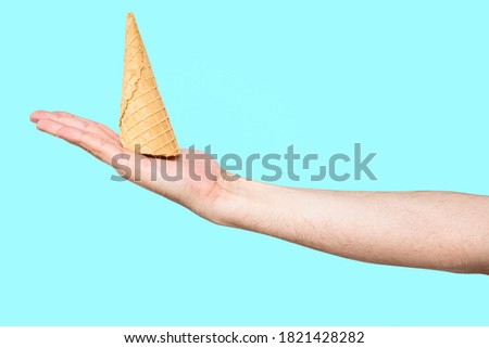 Ice cream cone in hand pastel blue background. Concept of eating ice cream. A man holds a waffle without ice cream in his hand on a different light background.