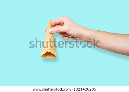Ice cream cone in hand pastel blue background. Concept of eating ice cream. A man holds a waffle without ice cream in his hand on a different light background.