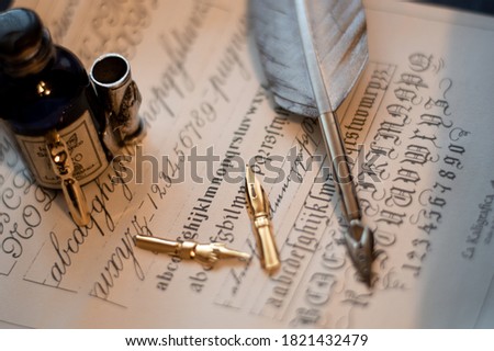 Photograph of a fountain pen with an old inkwell and several differently shaped nibs on papyrus with examples of calligraphy