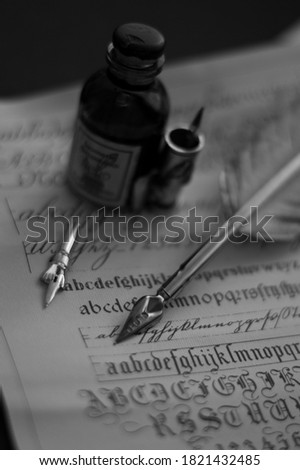 Photograph of a fountain pen with an old inkwell and several differently shaped nibs on papyrus with examples of calligraphy