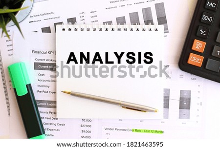 Notepad with text ANALYSIS on a white background, near calculator and office supplies.