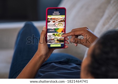 Woman lying on couch using food delivery app on smartphone. Close up of african woman hands holding cellphone and ordering food online. Royalty-Free Stock Photo #1821464741