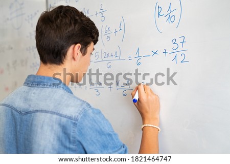 Back view of high school student solving math problem on whiteboard in classroom. Young man writing math solution on white board using marker. College guy solving math expression during lesson. Royalty-Free Stock Photo #1821464747