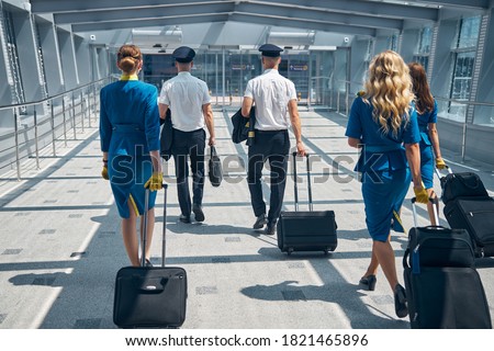 Flight attendants and pilots with trolley luggage bags heading to exit of airport terminal Royalty-Free Stock Photo #1821465896