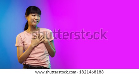 Asian young woman's portrait on gradient studio background in neon. Beautiful female model in casual style. Concept of human emotions, facial expression, youth, sales, ad. Flyer
