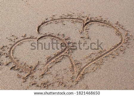 Two hearts drawn by finger or stick on sandy beach. One small woman's heart and one huge man's heart pictures on sand. Valentine's Day concept. Hand drawing hearts on sand, two hearts shaped on sand.