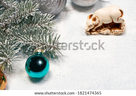 New Year's card with the symbol of 2021 - a bull on a snow-covered white background with a spruce twig decorated with a toy. Copyspace for text