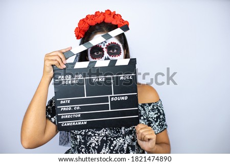 Woman wearing day of the dead costume over isolated white background holding clapperboard very happy having fun