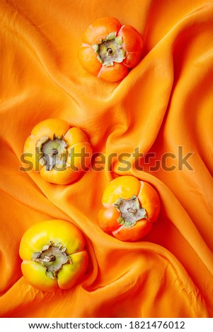 still life with persimmons on orange textile. vertical image. selective focus