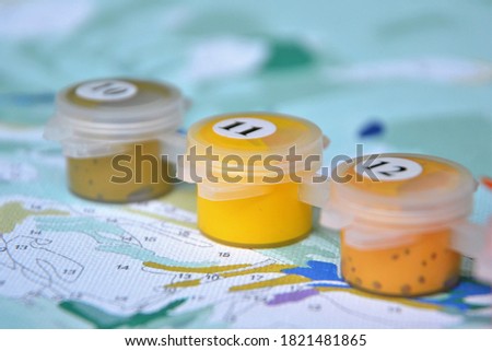 Painting by numbers, creative hobby. Small jars filled with paint on a painted canvas. DIY. Set to paint the picture with canvas and paints in different colors. Closeup, selective focus