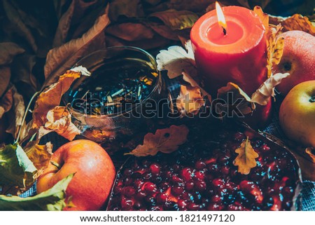Autumn picture with yellow dry leaves, herbal warm tea, lit candle and berry pie