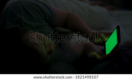 Close up of digital cell phone with green screen and a man in bed. Concept. Sleepy man using his smartphone and trying to sleep, concept of phone addiction and insomnia.