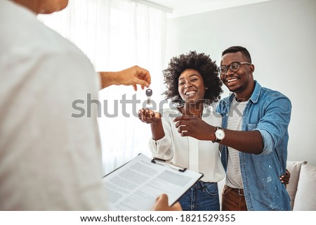 Photo of a smiling young couple thanking to the agent for the new house. Homeowners receiving their new house keys. Close up of a happy homeowners receiving their new house keys from a estate agent
