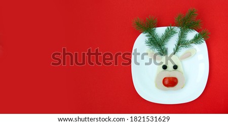 Funny Christmas sandwich for a child or party in the form of deer (sausage, bread, vegetables). With branches of Christmas trees and decorations, top view, copy space