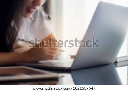 Blurred image of young positive asian girl work on laptop computer, hand holding electronics pen with digital tablet on the desk at home. Online education or e learning concept. 