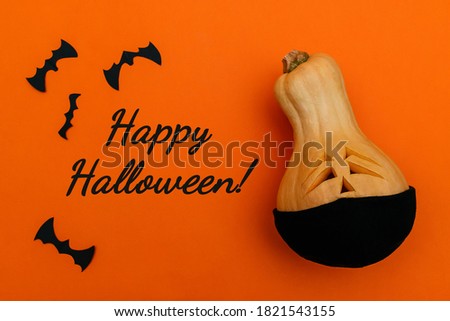 Halloween pumpkin in black protective medical mask and bats from black paper on orange background.Inscription HAPPY HALLOWEEN! on an orange background.Halloween and covid-19 concept.