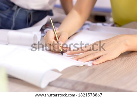 Fashion designer's hands. Closeup of hands drafting a new sewing pattern on paper, tailor working with a pencil, ruler, fabric, tool. Textile industry, hobby, workspace. Creation process. Drawing