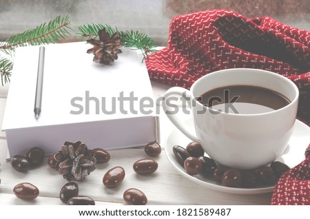 White cup of coffee with chocolates stands on a white window sill against the window