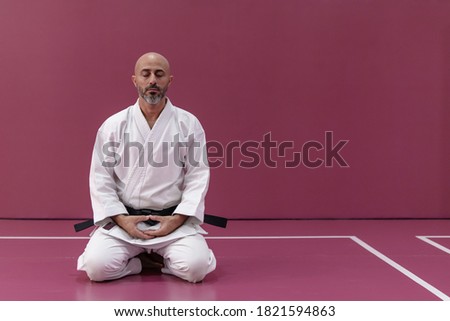 Karate master with black belt rank, in meditation position in his dojo or martial arts school Royalty-Free Stock Photo #1821594863