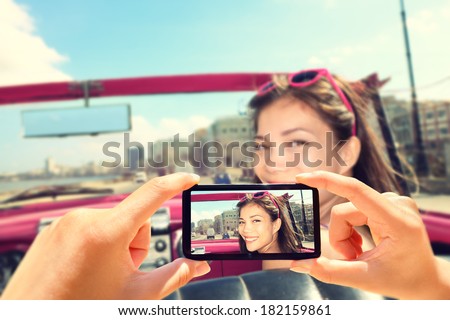 Taking pictures with smart phone of woman in car. Close up of camera phone showing photo of happy smiling woman driving in retro car.