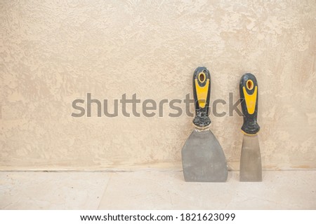 small and medium spatula on a wall background. Decorative plaster in golden beige color.