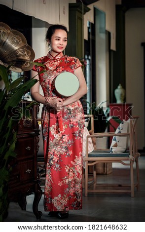 A woman in qipao stands next to an ancient phonograph and listens to music.Retro color card style