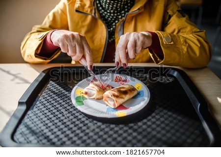 An aged woman dines in a cafe. The pensioner eats pancakes. Crop
