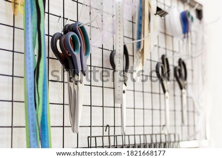 Professional tailor's tools hanging on the wall in the workshop. Scissors, measuring tapes, rules. Sewing tools. Manufacturing goods and clothes, craft products. Textile factory, atelier, sewing class
