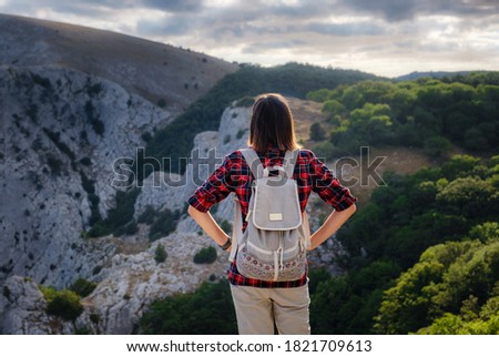 Fit female hiker with backpack and poles standing on a rocky mountain ridge looking out peaks in a healthy outdoors lifestyle concept