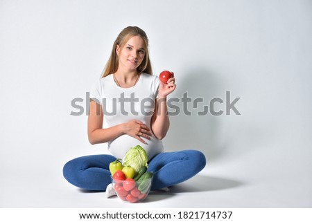 Pregnant woman sitting on a white background and fresh vegetables in a bowl