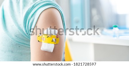 Vaccination of little girl in doctor's office.Kids funny adhesive plaster,gauze napkin.Sits on chair.Vaccine for covid-19 coronavirus,flu,infectious diseases.Injection.Clinical trials for human,child. Royalty-Free Stock Photo #1821728597
