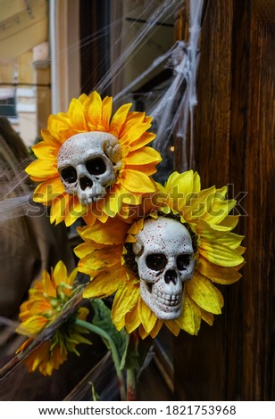 Decoration with skulls, flowers and cobwebs for the holiday of Halloween. Death symbolism in decorating the photo zone for All Saints Day. Bouquet of orange sunflowers with white skulls cores