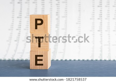 concept image a wooden block and word PTE - Foreign Language exams - with shadow selective focus a row of blocks is located on a grey notepad. Background of columns of numbers, front view.