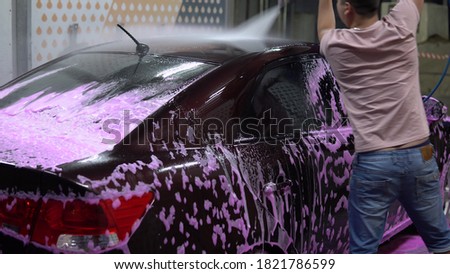 The man washes the car. Washes away pink foam with high pressure water