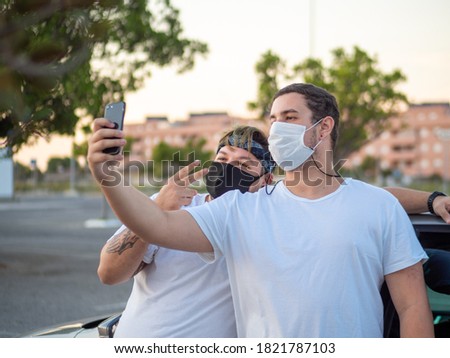 young men with tattoos taking selfies photos with their mobile phone leaning on a car