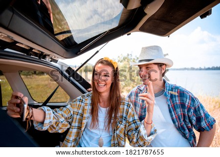 Young Couple posing for Selfie Picture in their Car Trunk in Nature. Sharing Image from the trip to their friends on social media. Video call chat from excursion
