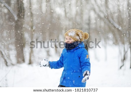 Little boy having fun playing with fresh snow. Snow fight. Kid dressed in a warm clothes, hat, hand gloves and scarf. Active outdoors leisure for child on nature in snowy winter day.
