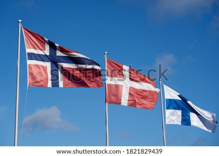 Flags of Nordic countries Norway, Denmark and Finland against a blue sky.            
